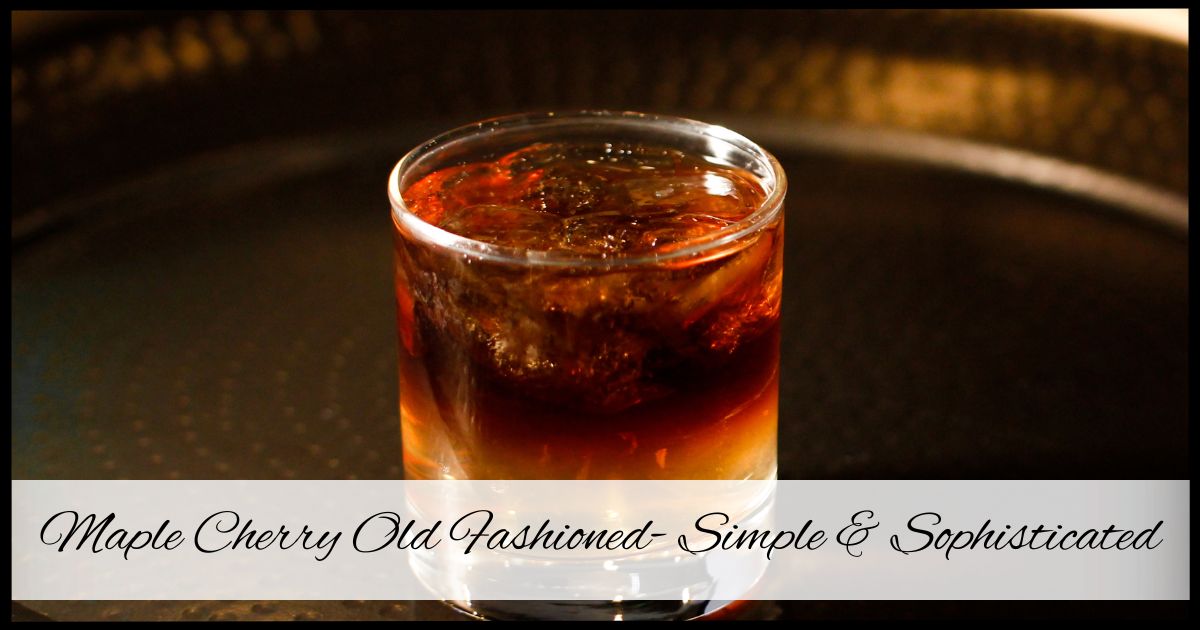 A glass of Maple Cherry Old Fashioned with an Amarena cherry garnish, rich amber whiskey, and ice, set against a warm, cozy backdrop.